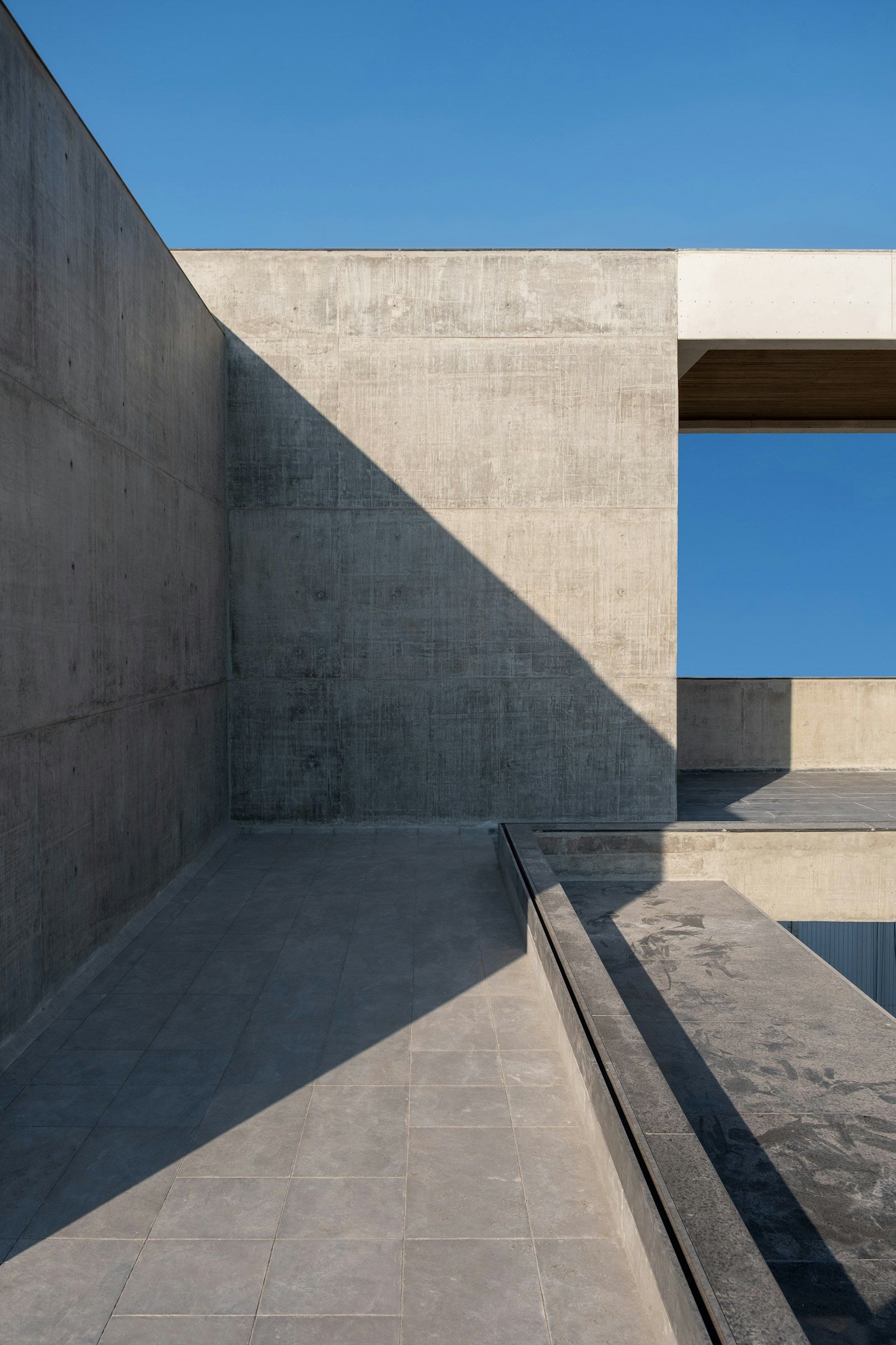 A sunlit concrete courtyard with a framed view of the sky